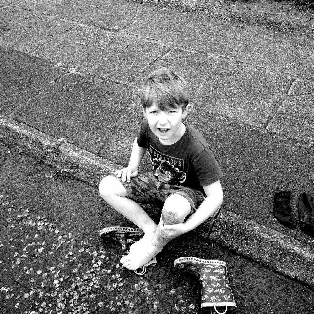 Boy sitting on the pavement with wellies off